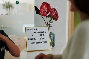 Empfang einer Patientin am Empfangstresen unserer Zahnarztpraxis mit Blumen im Hintergrund